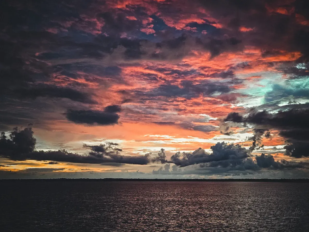 Diving Raja Ampat Indonesia Travel Photos 05 by Lynn Peiffer A pink, orange, and yellow sky over a dark but calm sea as the sun sets in Raja Ampat, Indonesia.