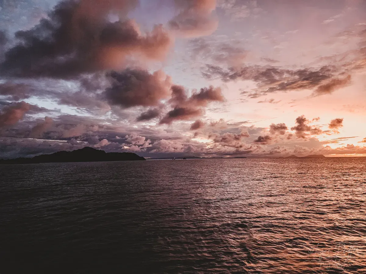 Diving Raja Ampat Indonesia Travel Photos 10 by Lynn Peiffer Clouds dot the pink sky during sunset over the dark sea on a liveaboard in Raja Ampat, Indonesia.