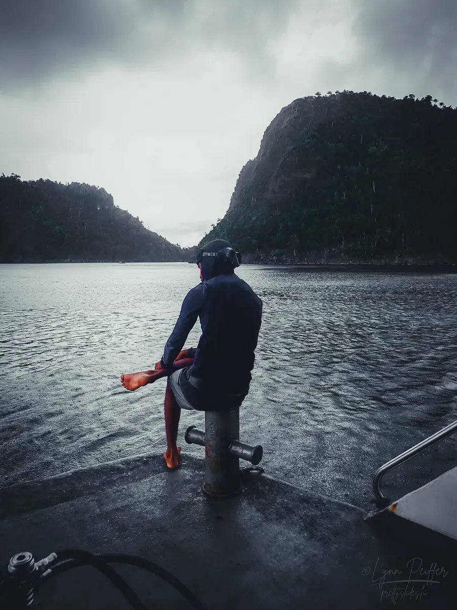 Diving Raja Ampat Indonesia Travel Photos 19 by Lynn Peiffer A portrait of a dive guide sitting on a ship with the ocean and limestone karsts in the background.