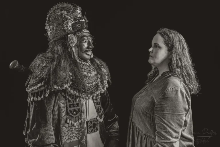 A portrait of Lynn Peiffer facing a Balinese man dressed in an elaborate Topeng Keras costume.