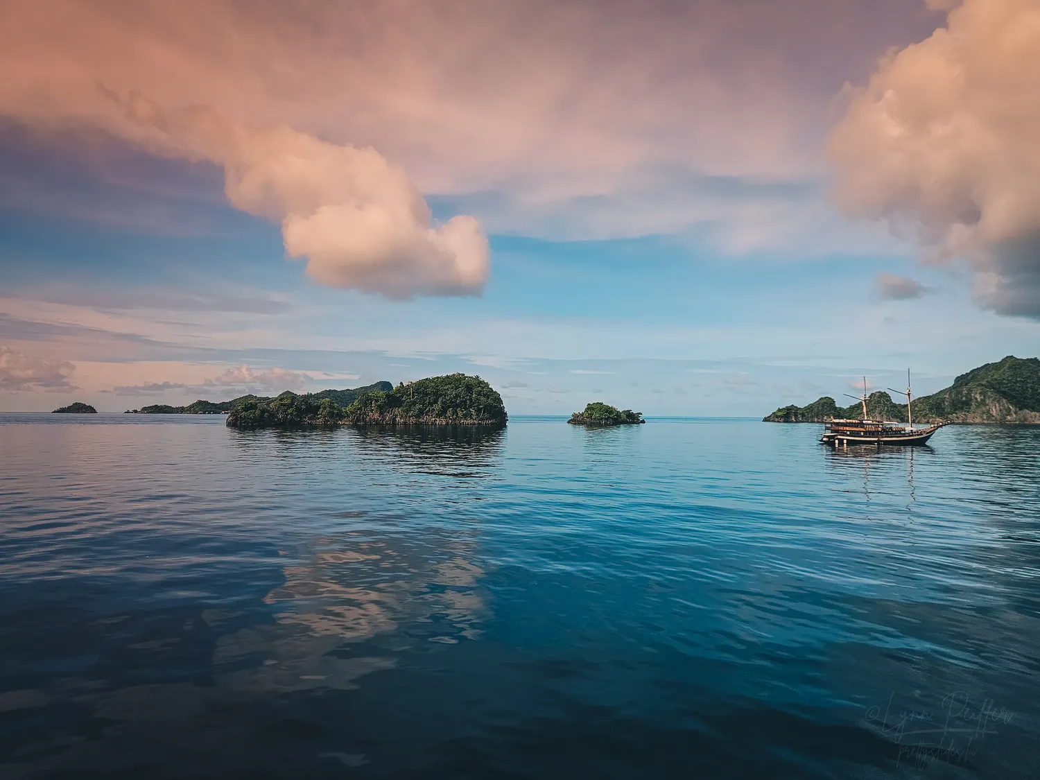 Places of Indonesia Landscape Travel Photos 01 by Lynn Peiffer A phinisi and small green islands create a stunning sunrise landscape in Raja Ampat, Indonesia.