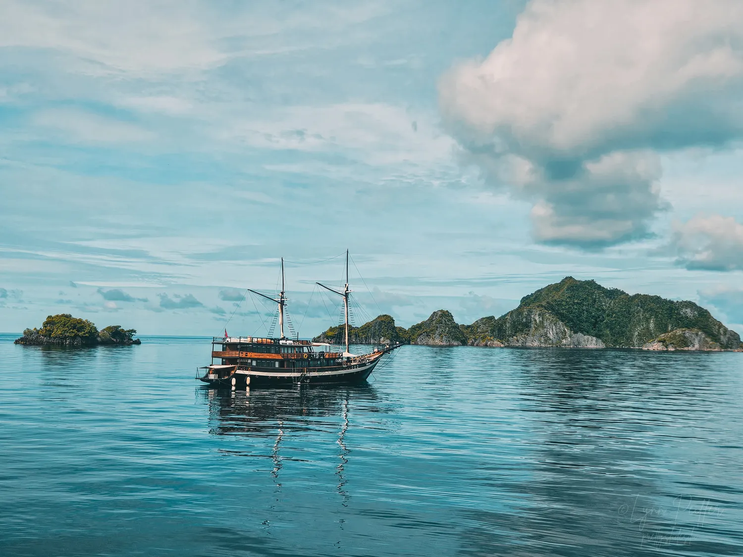 Places of Indonesia Landscape Travel Photos 02 by Lynn Peiffer A phinisi liveaboard rests in the calm waters amongst lush islands in Misool, Raja Ampat, Indonesia.