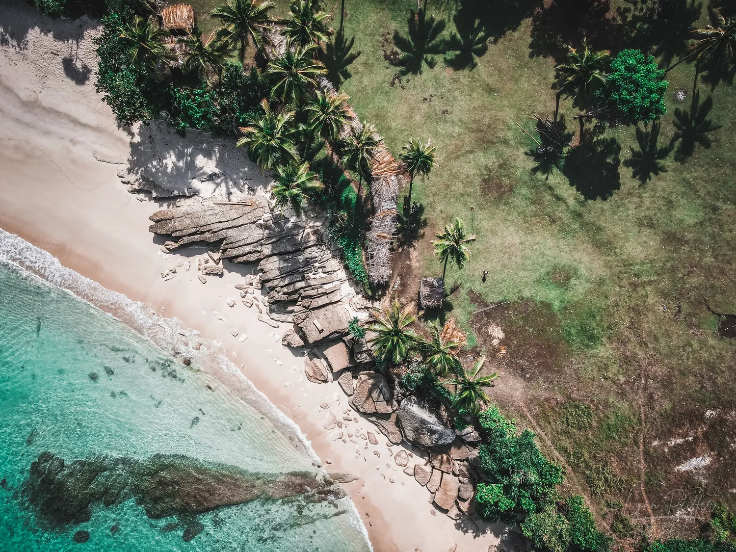 Places of Indonesia Landscape Travel Photos 07 by Lynn Peiffer An aerial view of a white sand beach, turquoise sea, palm trees, and a grassy field in Sumba, Indonesia.