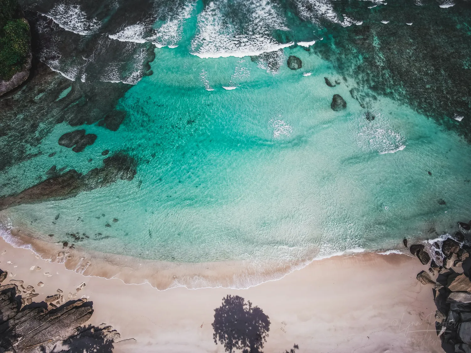 Places of Indonesia Landscape Travel Photos 08 by Lynn Peiffer An aerial view of clear turquoise ocean meeting a white sand beach in Sumba, Indonesia.