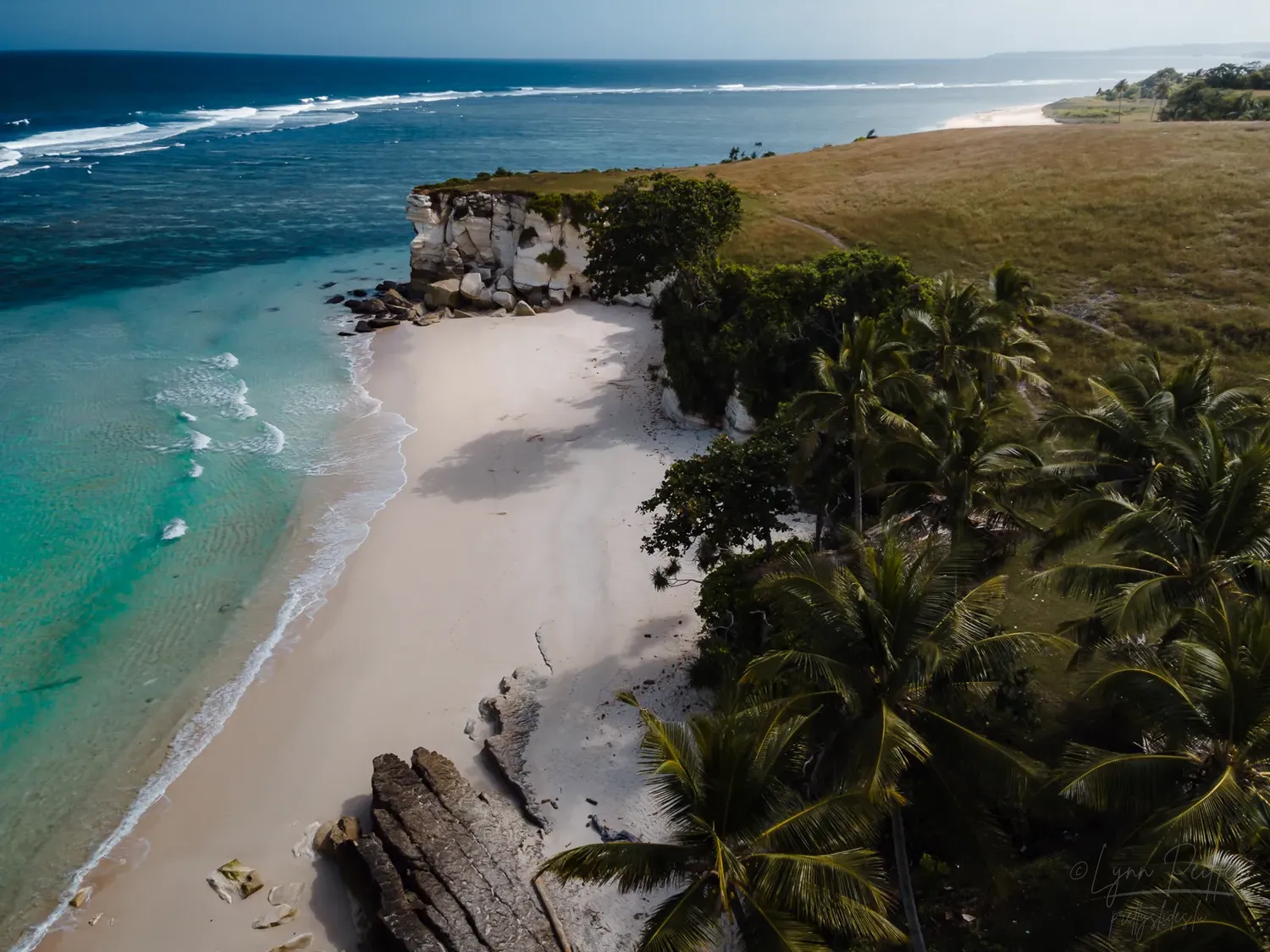 Places of Indonesia Landscape Travel Photos 11 by Lynn Peiffer The ocean meets a white sand beach and cliffs in Sumba, Indonesia.