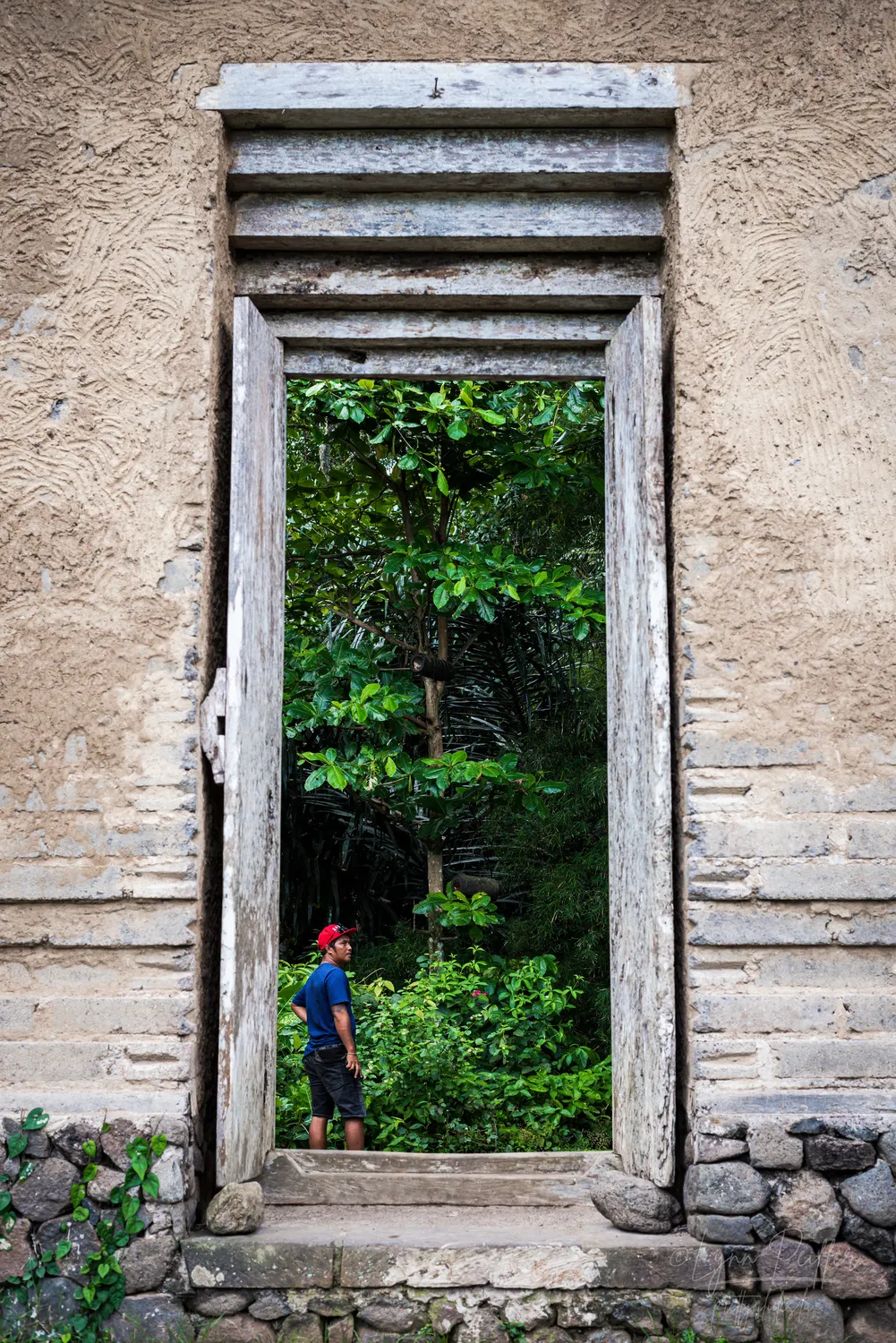 Places of Indonesia Landscape Travel Photos 34 by Lynn Peiffer A man is seen through a rustic doorway in a stone wall in Bali, Indonesia.